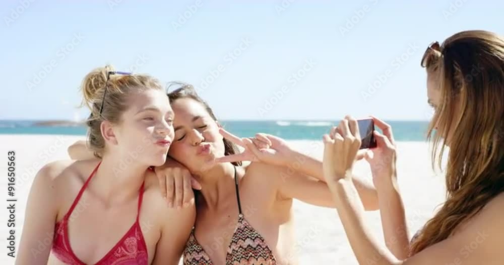 Three teenage girl friends taking photo on beach wearing colorful bikini sharing vacation photo Three teenage girl friends taking photo on beach wearing colorful bikini sharing vacation photo