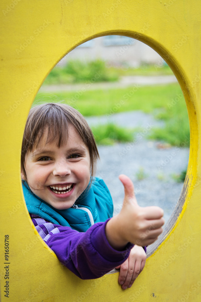 Cute smiling girl showing ok out of the window at the playground. Cute smiling girl showing ok out of the window at the playground.