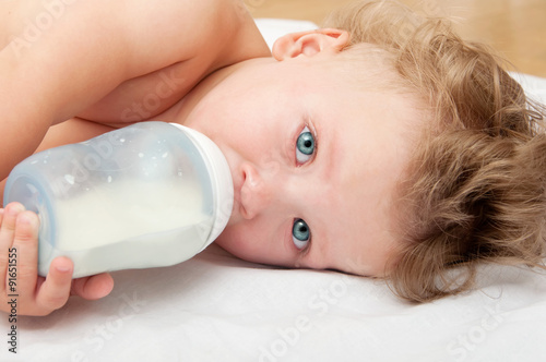  little curly-headed baby sucks a bottle of milk