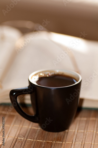 cup of coffee, standing next to an open book, on which lie glass