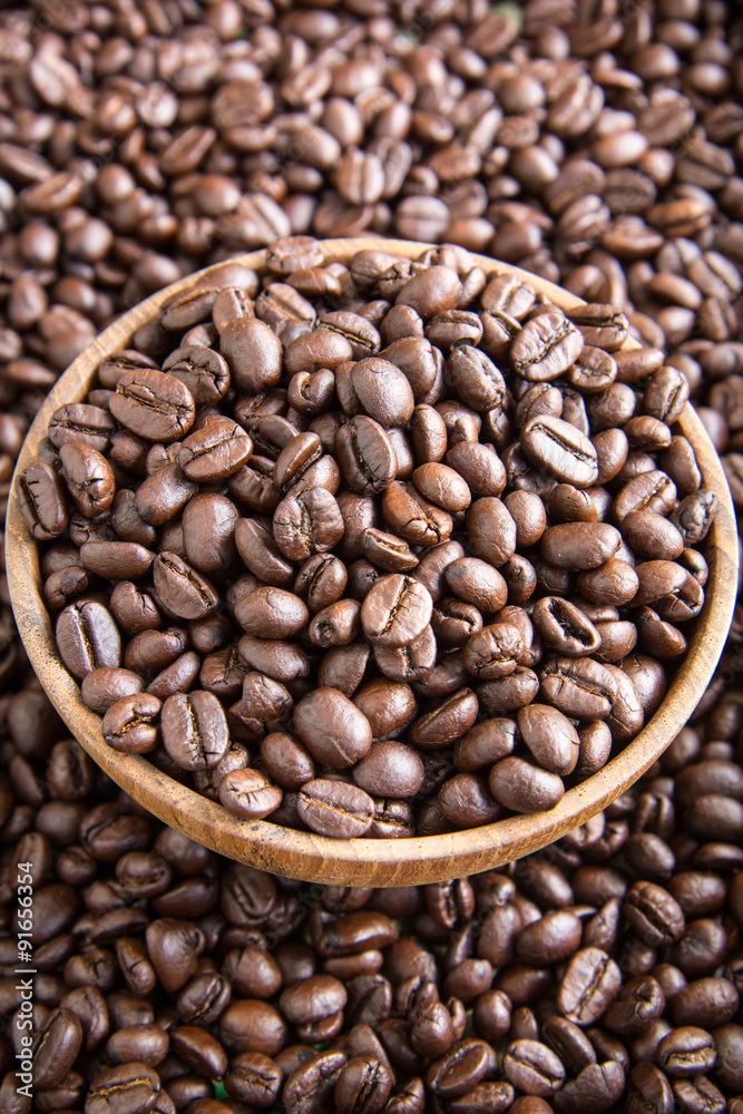 roasted coffee beans in wooden bowl with coffee background