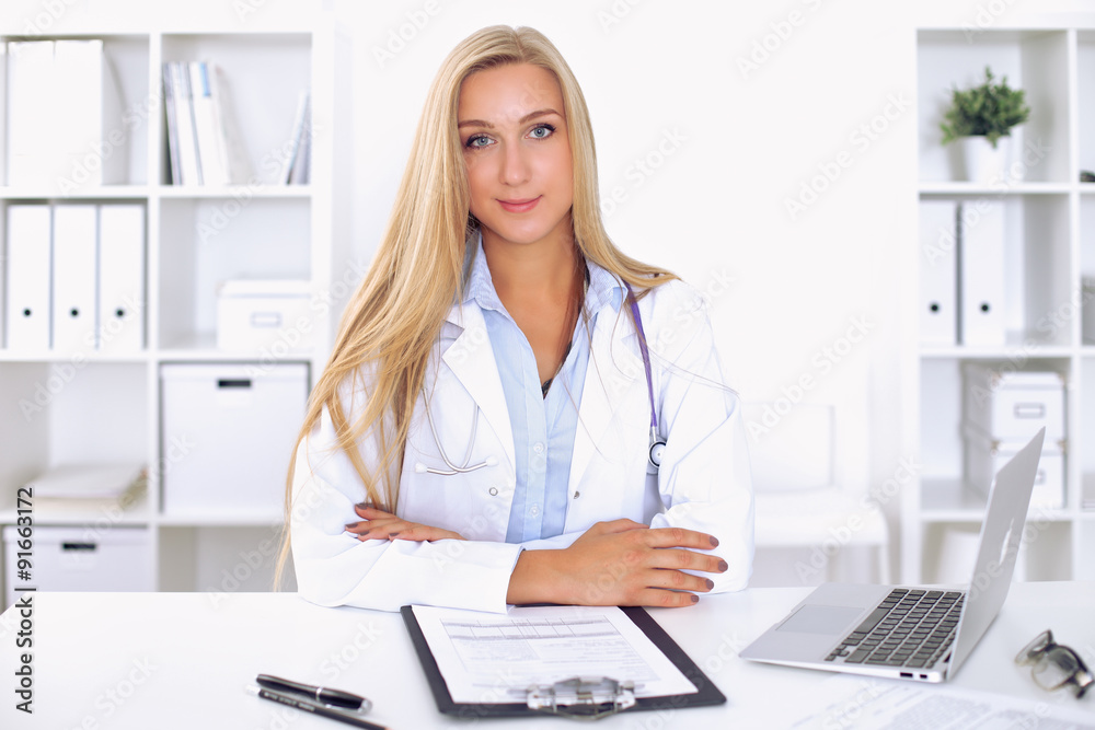 Blonde female doctor sitting at the table in hospital Blonde female doctor sitting at the table in hospital