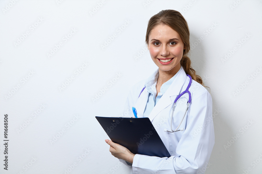 Friendly smiling young female doctor, standing near wall Friendly smiling young female doctor, standing near wall