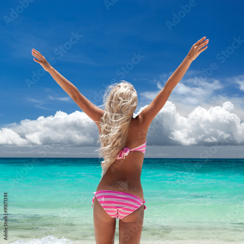 Woman in bikini with outstretched arms on tropical beach