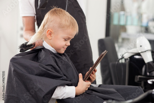 Professional young hairdresser is making hairstyle for child