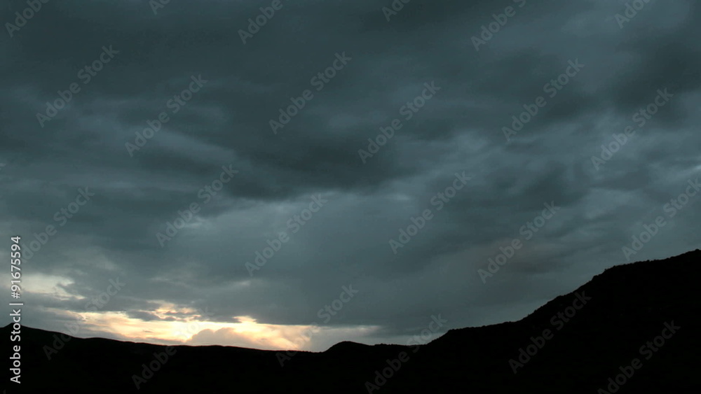 Slow pan as golden light flares at the horizon beneath dark storm clouds. Slow pan as golden light flares at the horizon beneath dark storm clouds.