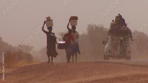 Women walk carrying goods on their heads through the Sahara desert in Mali.
