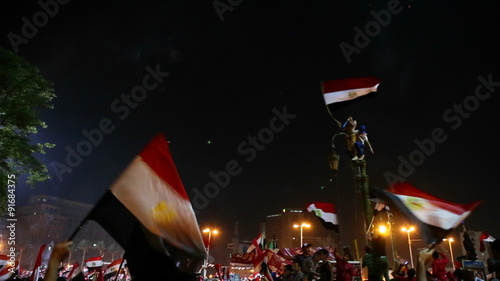 Protestors wave flags and fireworks go off at a nighttime rally in Cairo, Egypt. photo