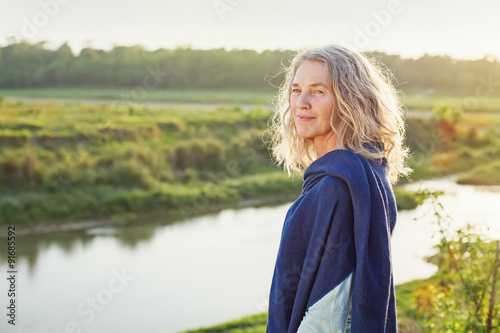 Beautiful mature woman standing in front of the river in autumn