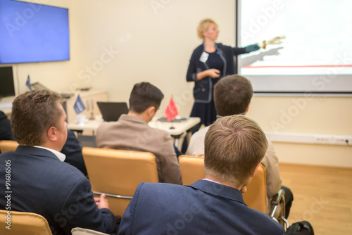 Photo of successful businesswoman reading lecture to his colleagues at presentation of new project and pointing on the white screen © elen31