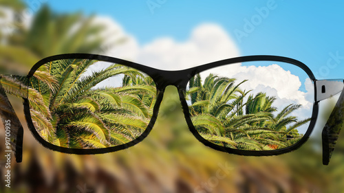 Put the glasses for the different, better view. Looking at the palms, clouds and sky.