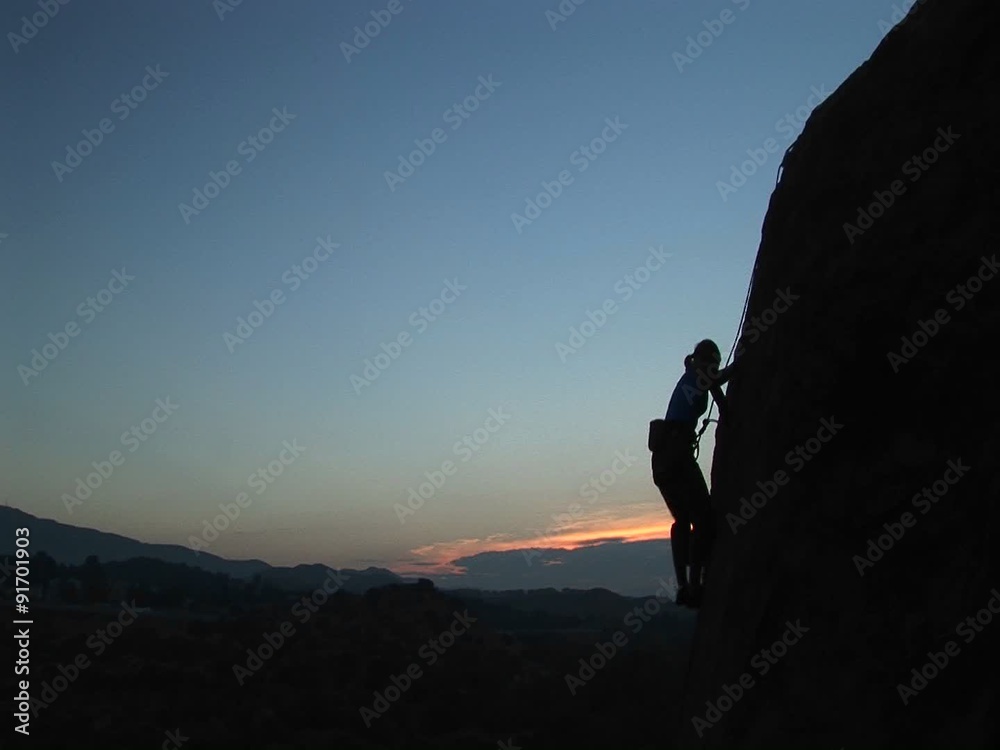 Long-shot of a rock climber scaling a cliff silhouetted against a golden-hour-sky.