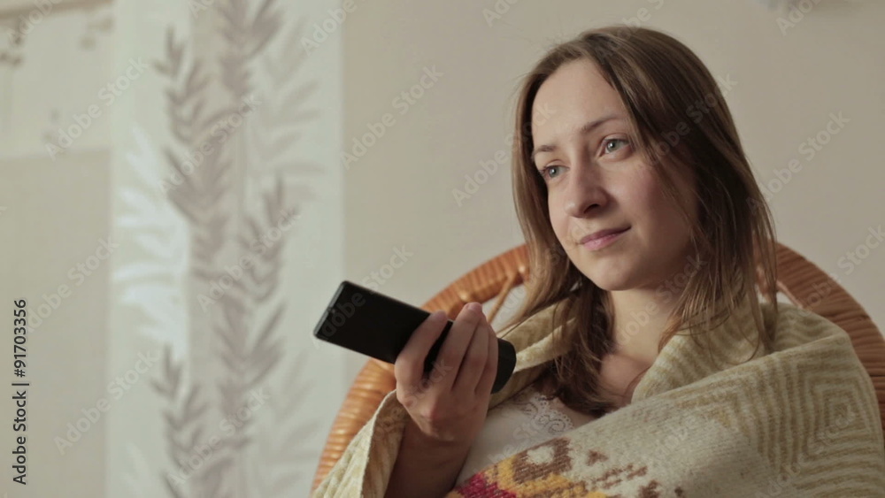 Young woman covered with blanket holding remote control and Young woman covered with blanket holding remote control and