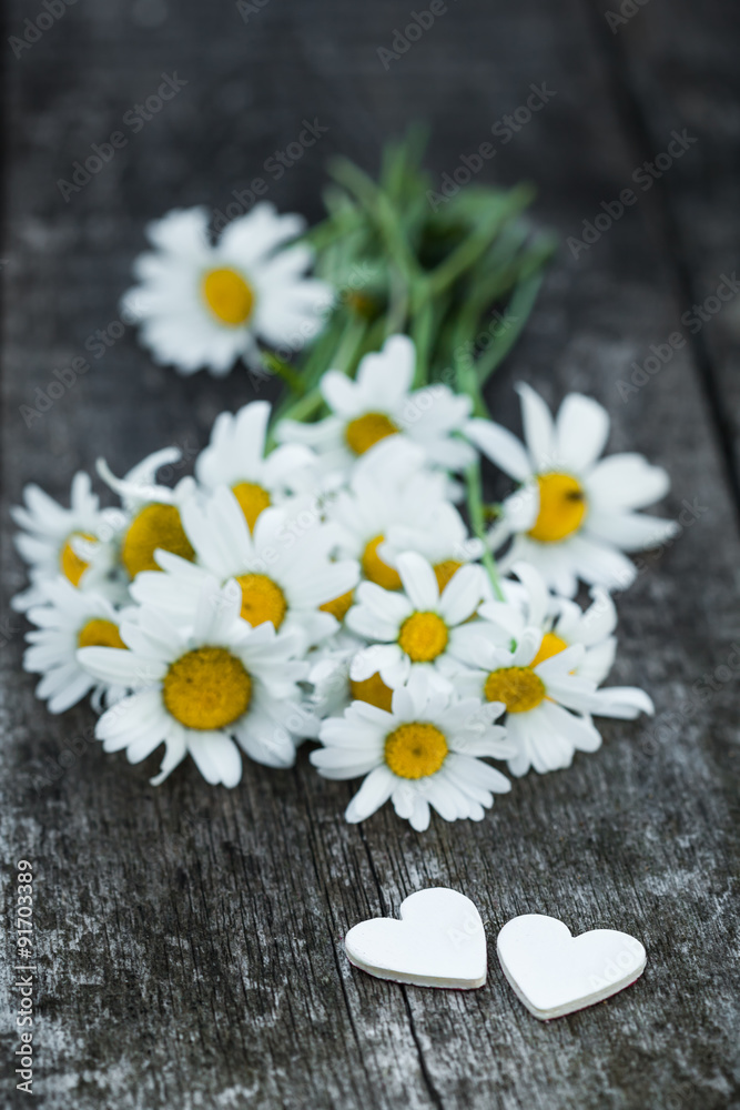 Beautiful fresh daisies decorated with hearts on wooden texture