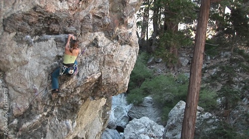 Pan-up of a rock climber making her way up a perpendicular rock cliff face.