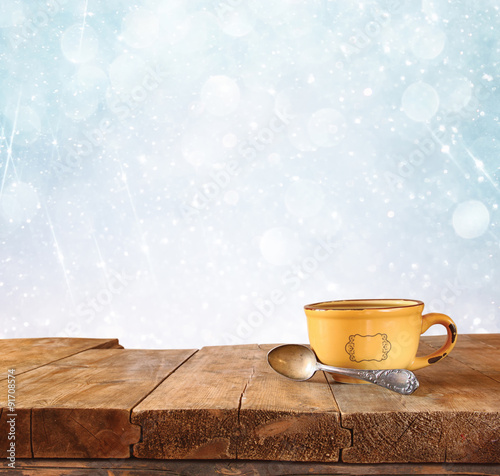 front image of coffee cup over wooden table in front of glitter background with glitter overlay  