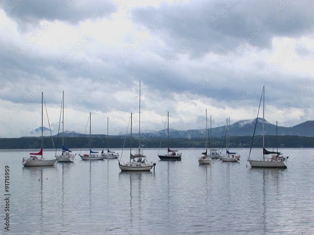 Clouds cover a mountain range in the distance of sailboats on calm water at Lake Champlain in Vermont. Clouds cover a mountain range in the distance of sailboats on calm water at Lake Champlain in Vermont.
