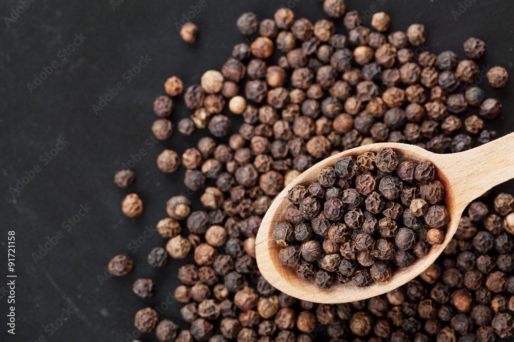 Closeup black pepper whole in wooden spoon on black stone table, top view Closeup black pepper whole in wooden spoon on black stone table, top view