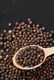 Closeup black pepper whole in wooden spoon on black stone table, top view