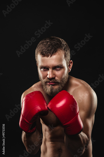 Athletic bearded boxer with gloves on a dark background