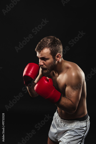 Athletic bearded boxer with gloves on a dark background © Nigrechok