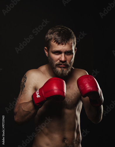 Athletic bearded boxer with gloves on a dark background