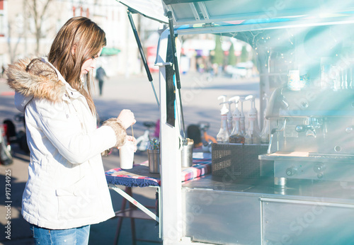 Young girl stirring coffee in cup on sunny street background