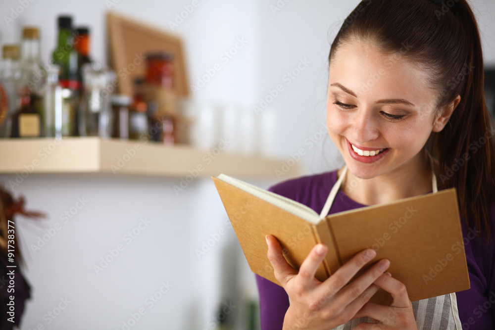 A young woman standing in the kitchen reading a cookbook. A young woman standing in the kitchen reading a cookbook.