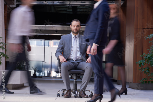 business man sitting in office chair, people group passing by