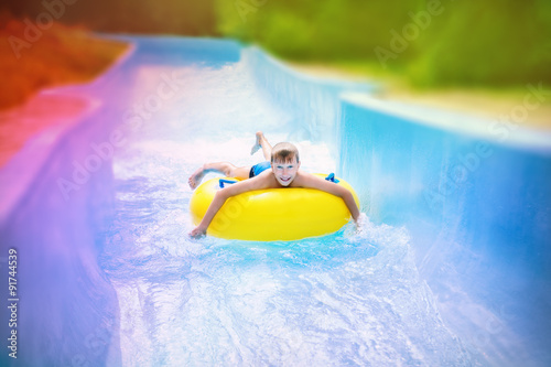 Funny excited child enjoying summer vacation in water park riding on slide with yellow float