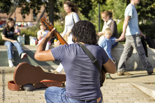 A street musician (busker) plays guitar for passersby.