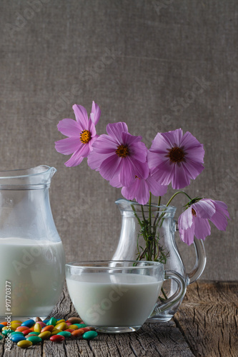 Cup of milk on wooden table with flowers and sweet dragees