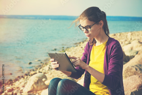 pretty girl using digital tablet at sunny sea stone coast