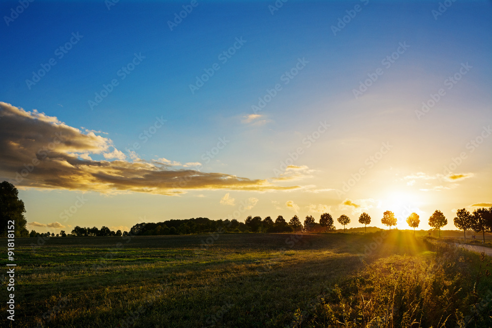 Fototapeta premium Sunset over a idyllic country landscape with fields and trees