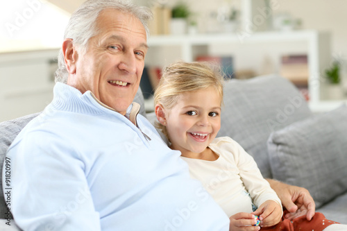 Portrait of grandfather with little girl sitting in couch