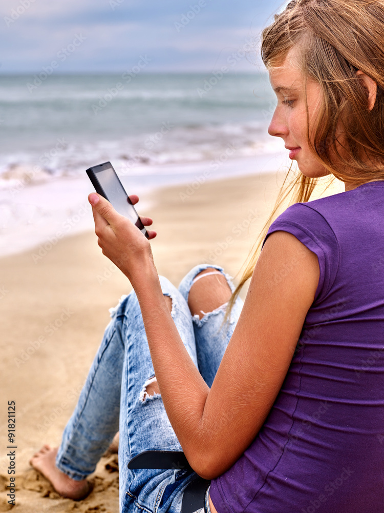 Girl with mobile phone sitting on sand near sea.