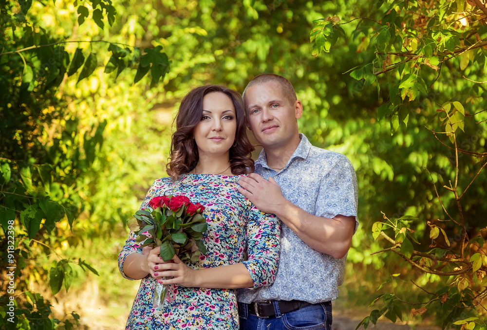 Happy loving couple hugging and posing in the park with bouquet of red roses