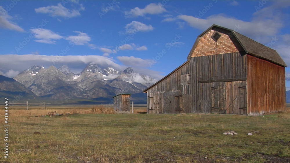 An old barn sits in a field with the Grand Teton mountain Range in the background An old barn sits in a field with the Grand Teton mountain Range in the background