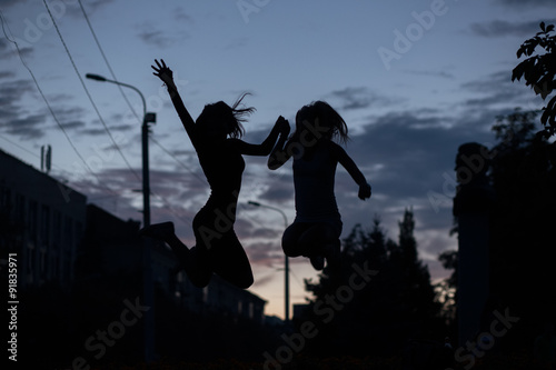 Silhouette of jumping girlfriends on the evening sky