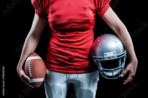 Mid section of sportsman holding American football and helmet