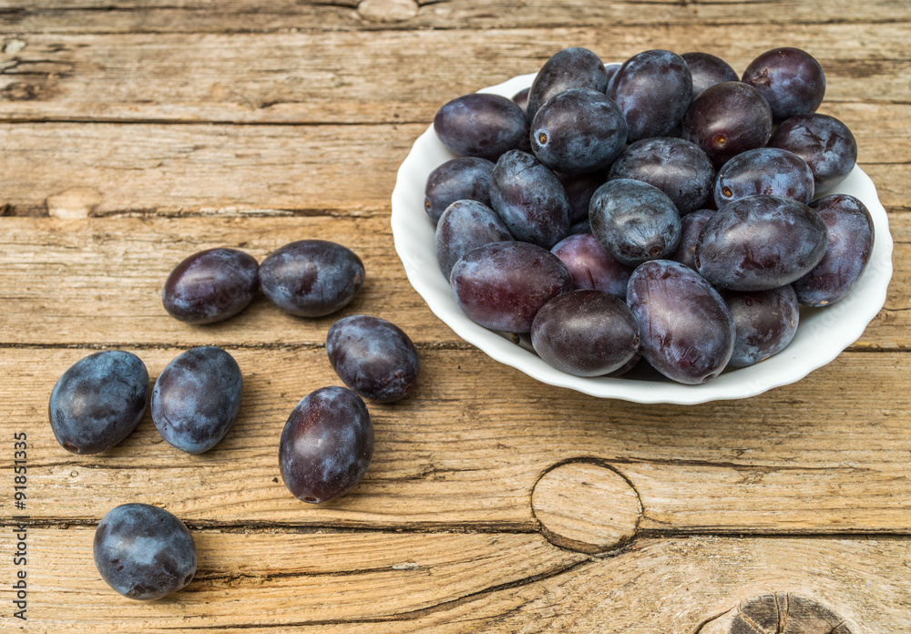 Fototapeta premium Plate full of fresh plums on a wooden background