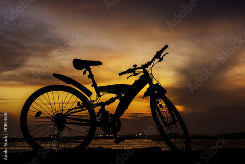 Silhouette of mountain bike parking on jetty beside sea with sun