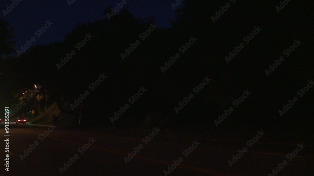 A car travels along a street at night in Los Angeles, California as seen through the rear window at an angle.