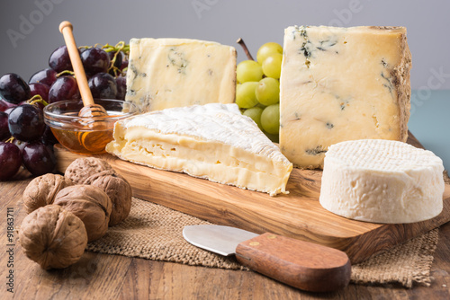 wooden board with cheeses, grapes, nuts and honey