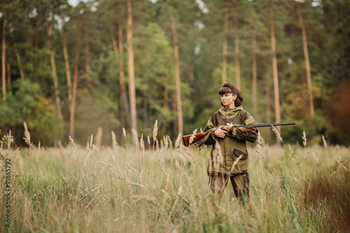 Young beautiful woman hunter with a shotgun in the forest