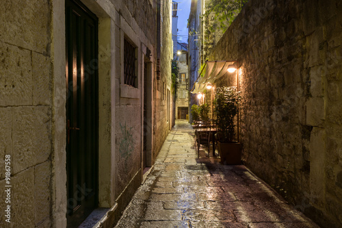 Narrow and empty alley with few cafe tables at the old town in Split  Croatia  at dark after rain.