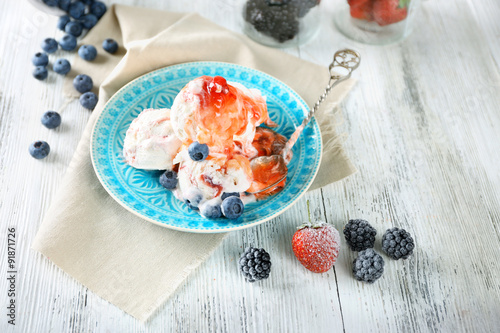 Delicious ice cream with fresh frozen berries and sauce, on color wooden background