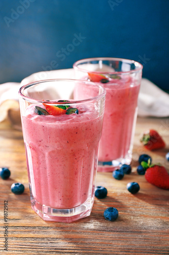 Glasses of berry smoothie on wooden table on dark background