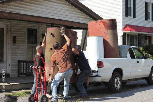 Men lifting a very heavy oil tank loading into truck