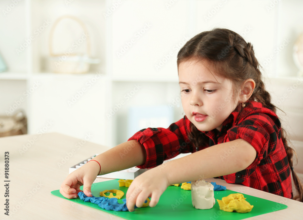 Cute little girl moulds from plasticine on table